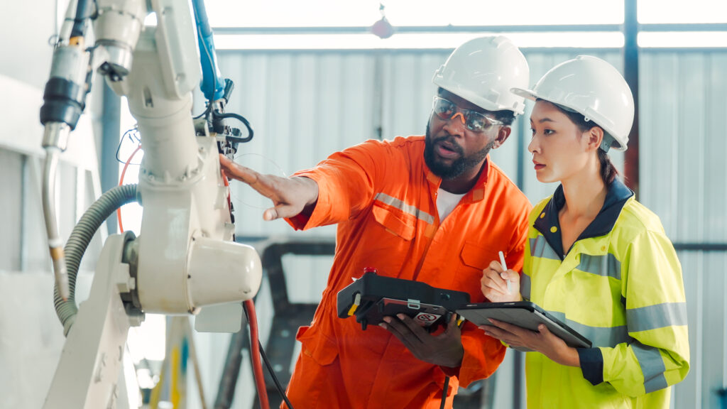 Two engineers in safety equipment discuss industrial machinery during workplace training.